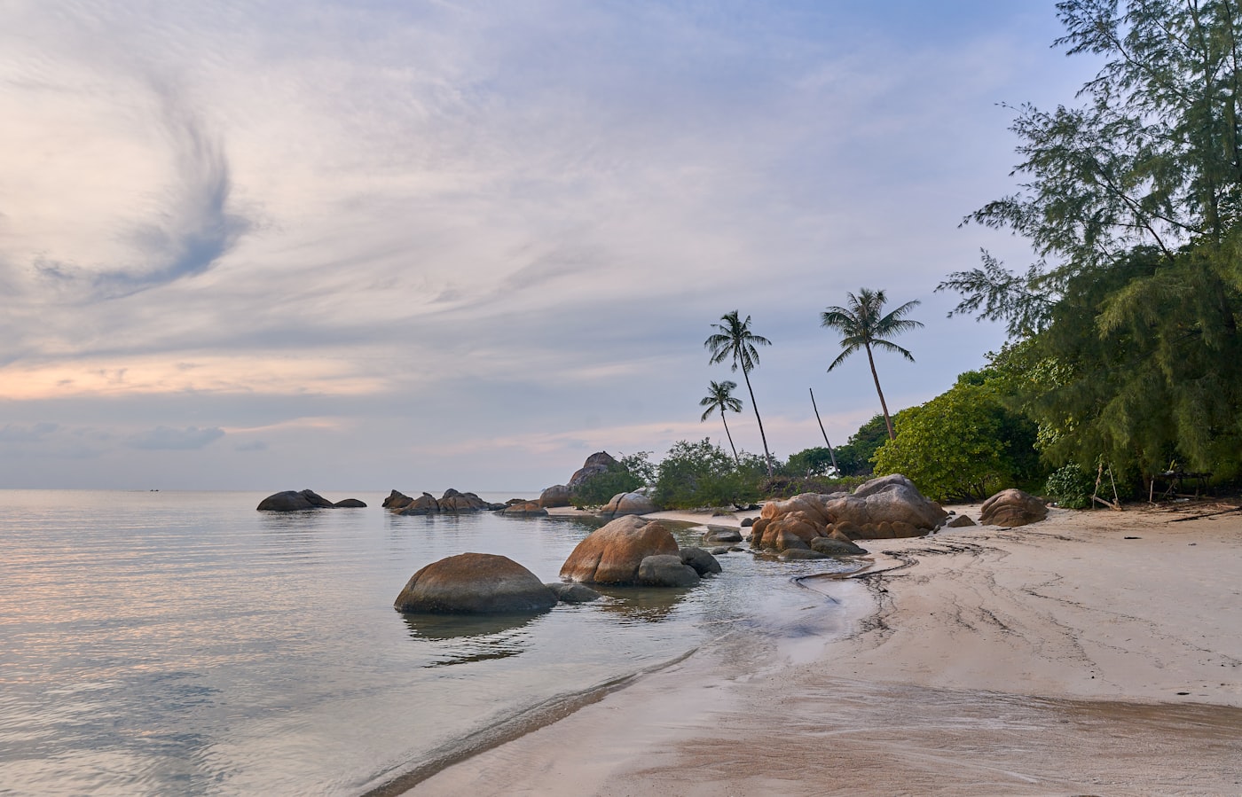 Granite boulders and coconut palms on a deserted Koh Phangan beach in flat evening light